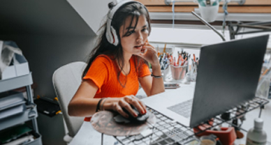 A focused teacher wearing headphones sits at a desk, engaged with her laptop.