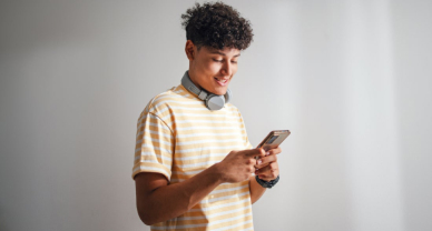 A young man smiles while holding a cell phone, ready to take an online test.
